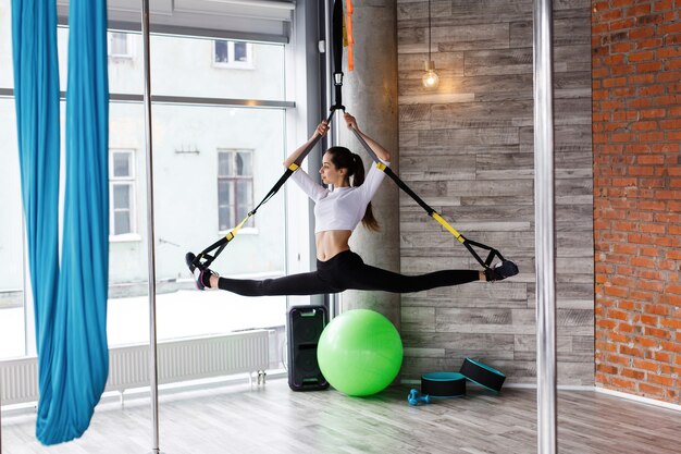 Geeignete junge Frau tut das Ausdehnen, drückt hoch und zieht auf die Gymnastikringe in der Turnhalle hoch