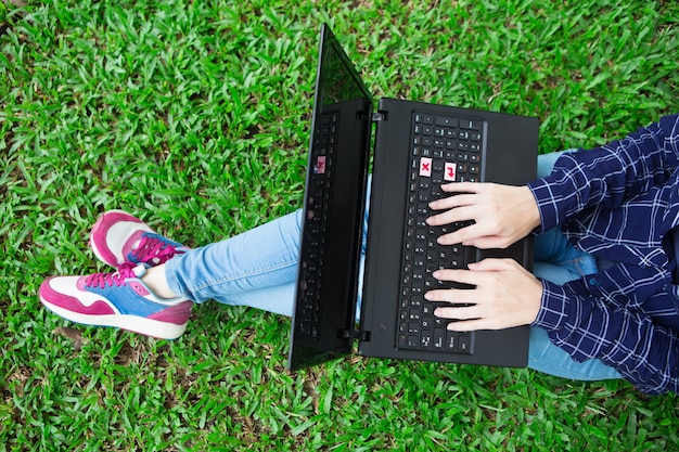 Geerntete Ansicht des Mädchens, das an Laptop auf Gras arbeitet