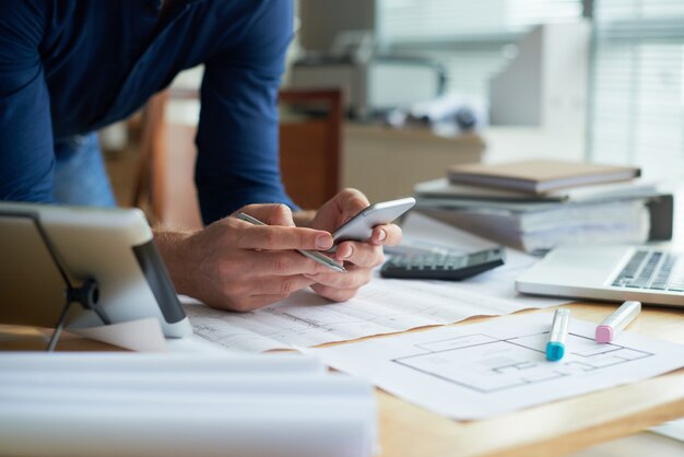 Geerntete unerkennbare Person, die mit Smartphone in den Händen sich lehnen auf dem Schreibtisch arbeitet