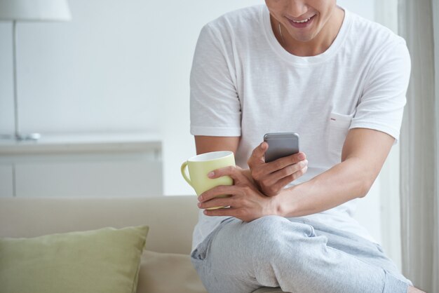 Geernteter Mann, der sein Telefon an einer Tasse Morgentee überprüft