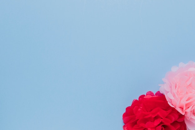 Kostenloses Foto gefälschte rosa und rote schöne dekorative blumen an der ecke des blauen hintergrundes