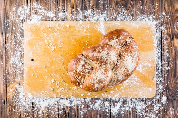 Geflochtenes Brot auf Schneidebrett mit ausgebreitetem Weißmehl