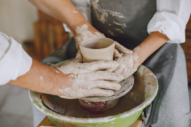 Gegenseitige kreative Arbeit. Erwachsenes elegantes Paar in Freizeitkleidung und Schürzen. Leute, die eine Schüssel auf einer Töpferscheibe in einem Tonstudio schaffen.