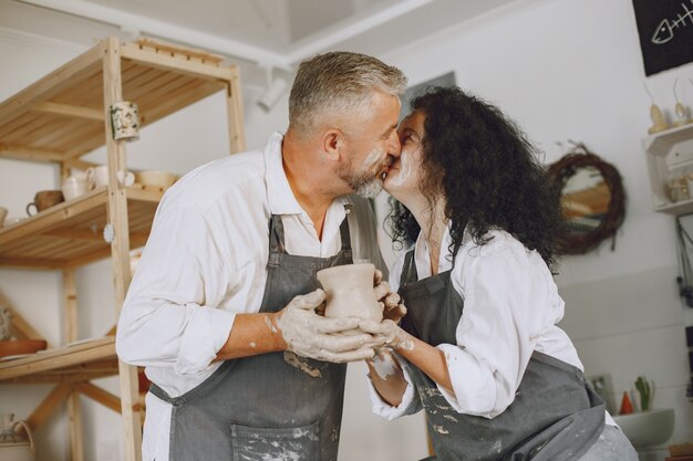 Gegenseitige kreative Arbeit. Erwachsenes elegantes Paar in Freizeitkleidung und Schürzen. Leute, die eine Schüssel auf einer Töpferscheibe in einem Tonstudio schaffen.