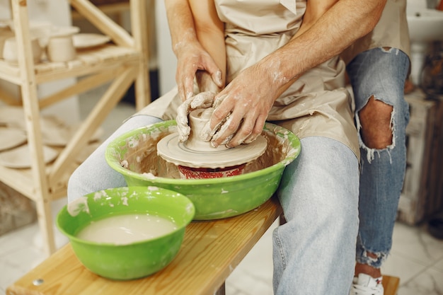 Gegenseitige kreative Arbeit. Junges schönes Paar in Freizeitkleidung und Schürzen. Leute, die eine Schüssel auf einer Töpferscheibe in einem Tonstudio schaffen.