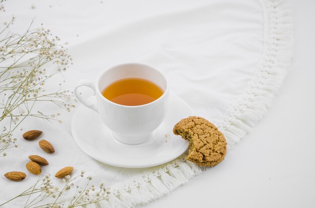 Gegessene Plätzchen und Mandeln mit weißer Kräuterteeschale auf Tischdecke