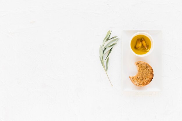 Gegessenes Brot mit Knoblauchzehe in der Ölschüssel auf weißem Hintergrund