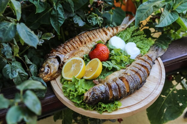 Gegrillte Fische auf dem Holzbrett Salat Tomaten Zwiebel Zitrone