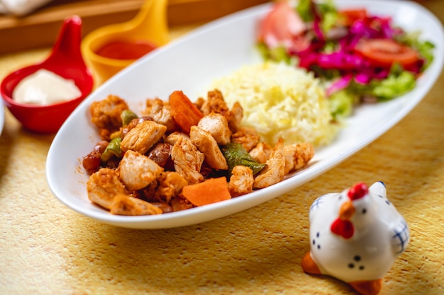 Gegrillte Hähnchenbrust mit Seitenansicht von Hühnchenragout mit Zwiebel-Karotten-Paprika-Gemüsesalat und Reisgarnitur auf einem Teller