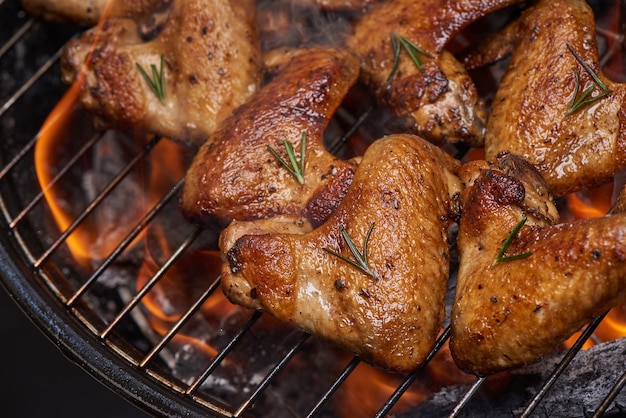 Gegrillte Hähnchenflügel auf dem brennenden Grill mit gegrilltem Gemüse in Barbecue-Sauce mit Pfeffersamen Rosmarin, Salz.