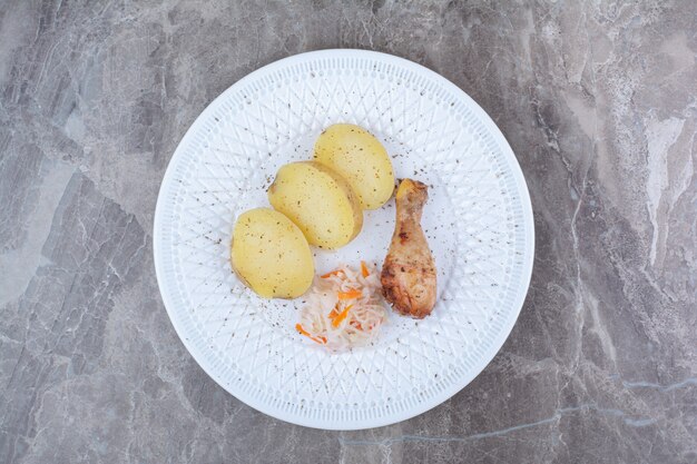 Gegrillte Hähnchenkeule, Kartoffel und Sauerkraut auf weißem Teller.