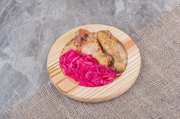 Gegrillte Hähnchenschenkel und eingelegter Kohl auf Holzteller.