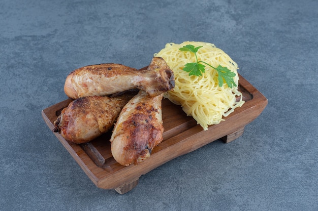 Gegrillte Hähnchenschenkel und Spaghetti auf Holzbrett.