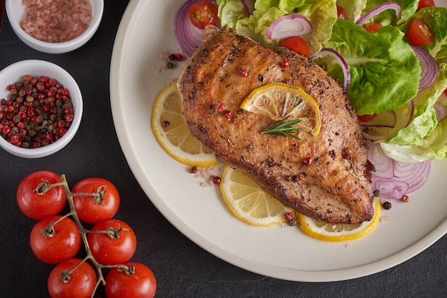 Gegrillte Hühnerbrust mit Salat Salat Tomaten, Kräutern, Zitrone, Rosmarin, Zwiebeln Zitrone auf Teller schneiden. Gesundes Mittagsmenü. Diätessen.