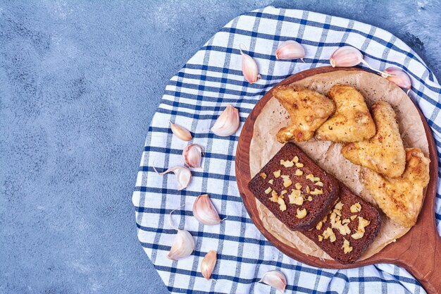 Gegrillte Hühnerflügel mit Schwarzbrot auf einem Holzbrett auf Blau