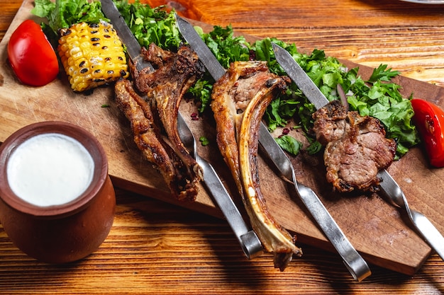 Gegrillte Lammrippen mit Anticot-Kebab von der Seitenansicht mit gegrilltem Mais und Joghurt der grünen roten Zwiebeltomate auf dem Tisch