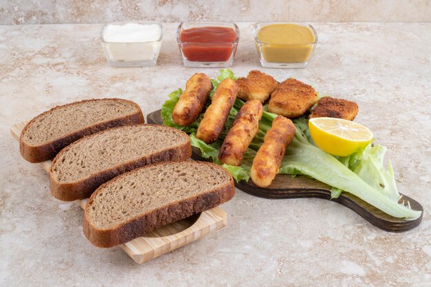 Gegrillte Würstchen mit Chicken Nuggets auf einem Stück Salat auf einem Holzbrett mit Saucen beiseite.