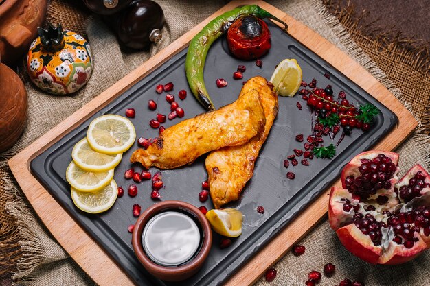 Gegrillter Fisch von oben mit Tomaten und gegrilltem Paprika mit Granatapfel-Zitronenscheiben und Narsharab-Sauce