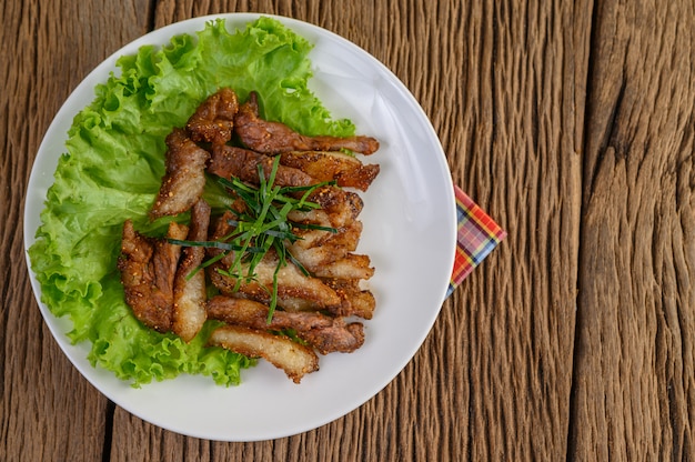 Gegrillter Schweinehals auf einem weißen Teller auf einem Holztisch.