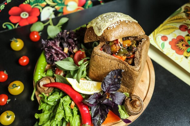 Gegrilltes Fleisch von oben mit Gemüse in einem Laib Graubrot mit Kirschtomatenpilzen und Kräutern mit Basilikum auf einem Ständer