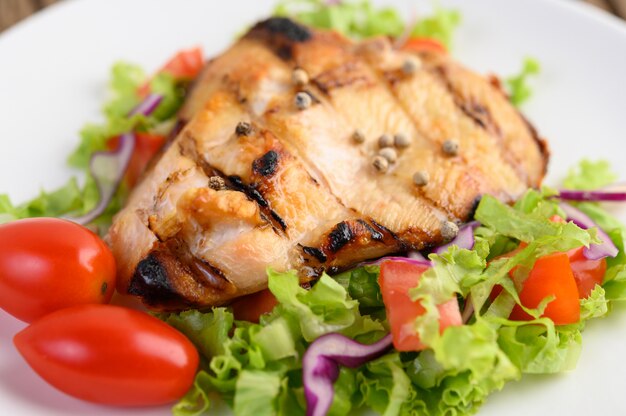 Gegrilltes Hähnchen auf einem weißen Teller mit einem Salat aus Tomaten, Karotten und Chilischoten in Stücke geschnitten.