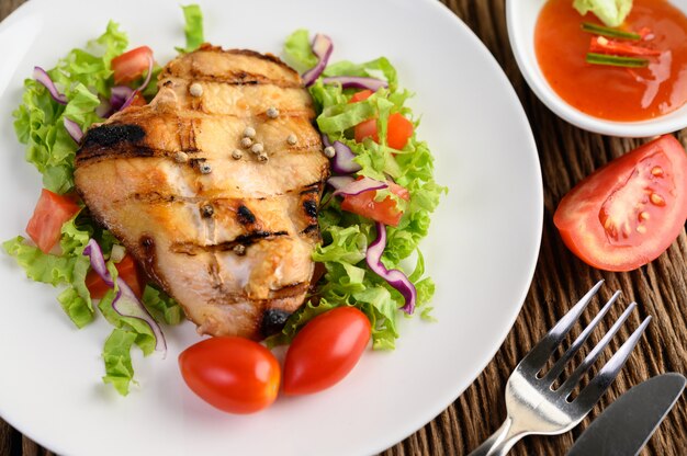 Gegrilltes Hähnchen auf einem weißen Teller mit einem Salat aus Tomaten, Karotten und Chilischoten in Stücke geschnitten.