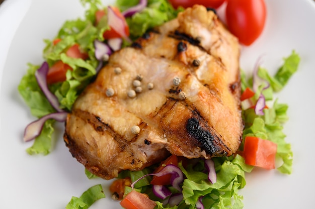 Gegrilltes Hähnchen auf einem weißen Teller mit einem Salat aus Tomaten, Karotten und Chilischoten in Stücke geschnitten.