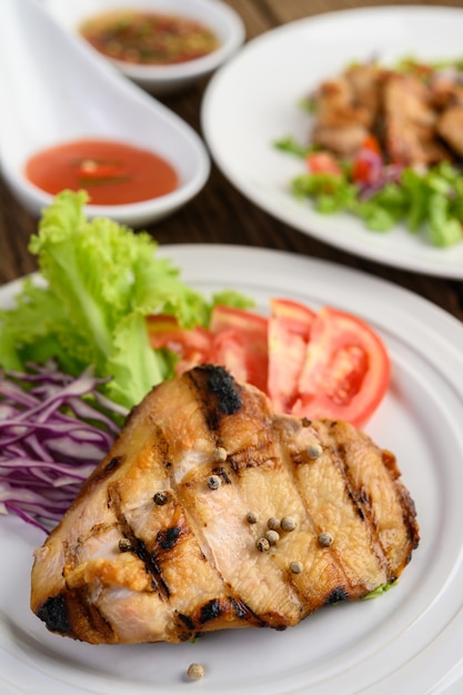 Gegrilltes Hähnchen auf einem weißen Teller mit einem Salat aus Tomaten, Karotten und Chilischoten in Stücke geschnitten.