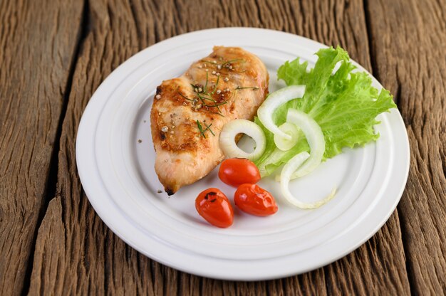 Gegrilltes Hähnchen auf einem weißen Teller mit Tomaten, Salat und Zwiebeln.