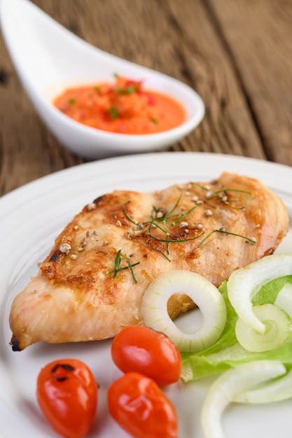 Gegrilltes hähnchen auf einem weißen teller mit tomaten, salat, zwiebeln, chili und sauce.