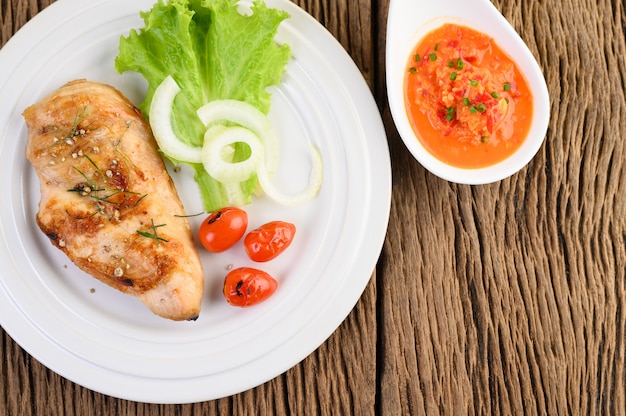 Gegrilltes Hähnchen auf einem weißen Teller mit Tomaten, Salat, Zwiebeln, Chili und Sauce.