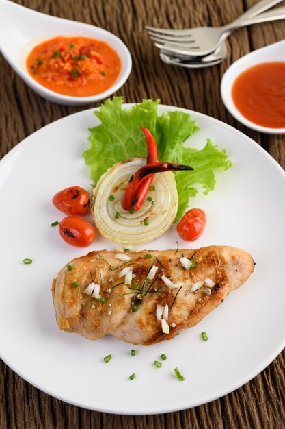 Gegrilltes Hähnchen auf einem weißen Teller mit Tomaten, Salat, Zwiebeln, Chili und Sauce.