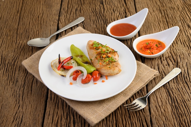 Gegrilltes Hähnchen auf einem weißen Teller mit Tomaten, Salat, Zwiebeln, Chili und Sauce.