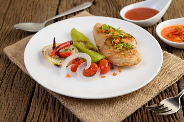 Gegrilltes Hähnchen auf einem weißen Teller mit Tomaten, Salat, Zwiebeln, Chili und Sauce.