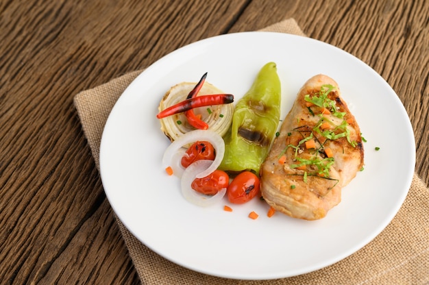 Gegrilltes Hähnchen auf einem weißen Teller mit Tomaten, Salat, Zwiebeln, Chili und Sauce.