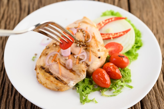 Gegrilltes Hähnchen auf einem weißen Teller mit Tomaten, Salat, Zwiebeln, Chili und Sauce.