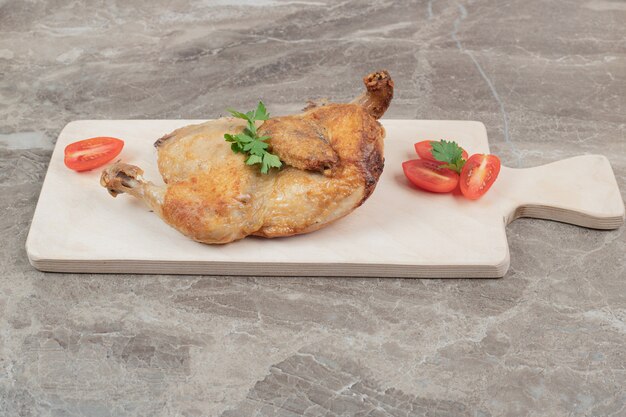 Gegrilltes Hähnchen auf Holzbrett mit Tomatenscheiben.