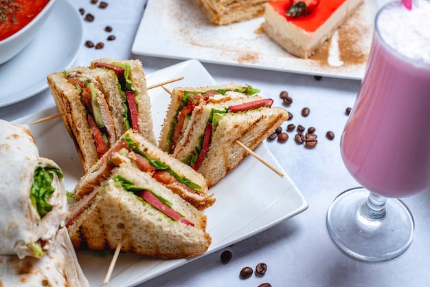 Gegrilltes Hähnchen mit Seitenansicht-Club-Sandwich mit Gurken-Tomatensauce, Salatmilchshake und Kaffeebohnen auf dem Tisch