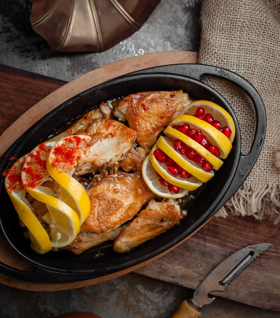 Gegrilltes Hähnchen mit Zitrone und Granatapfelkernen in schwarzer Eisenpfanne.