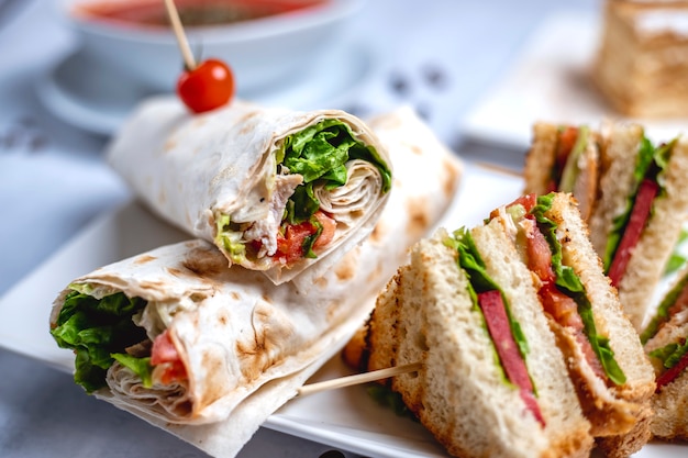 Gegrilltes Hähnchenfilet von der Seitenansicht mit Salatgrün-Mayo, eingewickelt in Tortilla- und Club-Sandwich auf dem Tisch