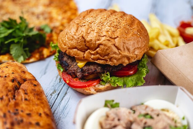 Gegrilltes Hamburger-Rindfleischpastetchen von der Seite mit Käsetomaten-Salat und Pommes Frites auf dem Tisch