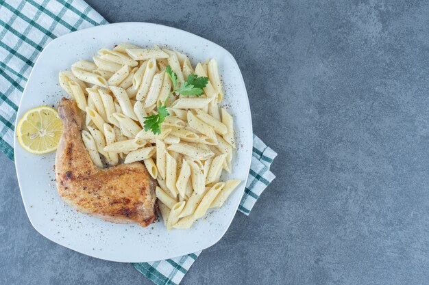 Gegrilltes Hühnerbein und Penne-Nudeln auf weißem Teller.