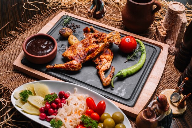 Gegrilltes Huhn auf Holzbrett mit Tomatenkartoffelpfeffersaucen Essiggurken Seitenansicht