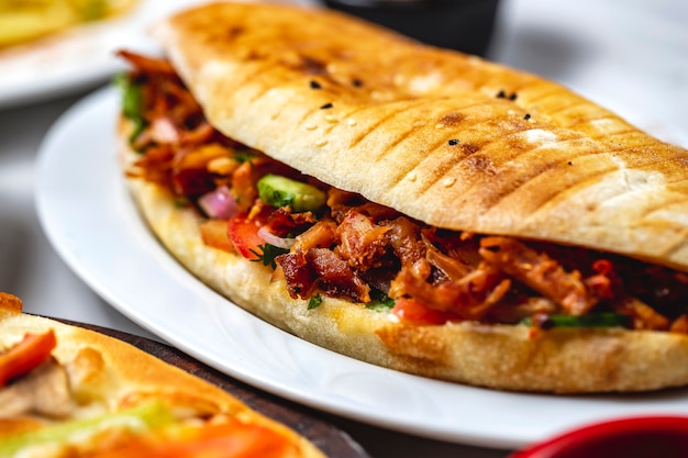 Gegrilltes Huhn der Seitenansicht-Hühnerdöners mit roten Zwiebeln der Gurken-Tomaten-Grüns und Soße in einem Brot