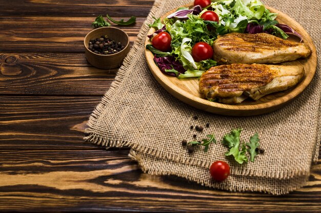 Gegrilltes Huhn und Salat in der Nähe von schwarzem Pfeffer