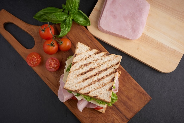 Gegrilltes Sandwich mit Schinken, Käse, Tomate und Salat auf Holzschneidebrett.