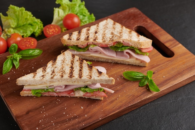 Gegrilltes Sandwich mit Schinken, Käse, Tomate und Salat auf Holzschneidebrett.