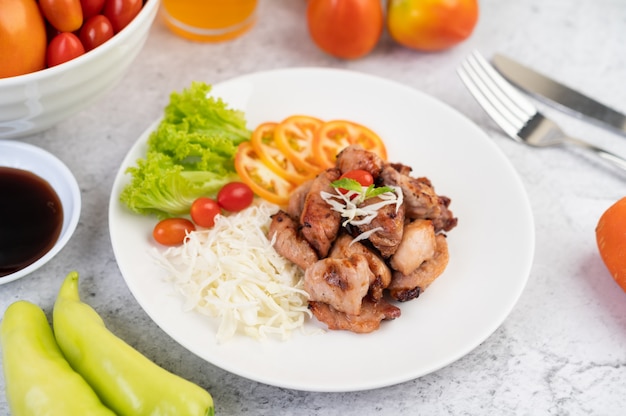 Gegrilltes Schweinekotelett mit Tomaten und Salat, in einer weißen Schüssel angeordnet.