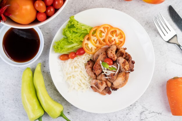 Gegrilltes Schweinekotelett mit Tomaten und Salat, in einer weißen Schüssel angeordnet.