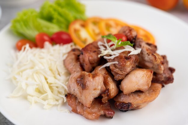 Gegrilltes Schweinekotelett mit Tomaten und Salat, in einer weißen Schüssel angeordnet.